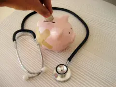 Salvadanaio a forma di maialino con cerotti, uno stetoscopio e una mano che inserisce una moneta. Simboleggia il dottore stipendio e la cura delle finanze.
