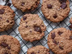 Saftige, vegane Kekse mit Schokoladenstückchen und grobem Salz bestreut, die auf einem Gitterrost abkühlen.