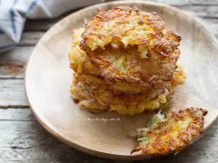 Una pila di dorate frittelle di patate, croccanti fuori e morbide dentro, servite su un piatto di legno.