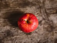 Czerwone jabłko z kroplami wody na drewnianym tle.