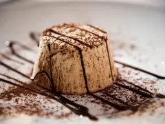 Delizioso parfait di mandorle, spolverato di cacao e decorato con scaglie di cioccolato fondente su un piatto bianco.