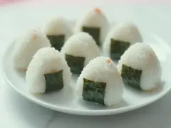 Kilka pysznych onigiri z łososiem, udekorowanych kawałkami nori, ułożonych na białym talerzu.