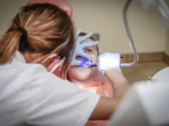 Dentysta w rękawiczkach bada zęby dziecka przy użyciu niebieskiego światła.