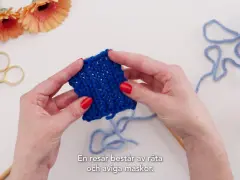 Händer som håller i ett stickat provstycke i resårstickning. Blått garn, sax och blommor syns i bakgrunden.