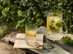 En glasburk med en alkoholfri drink, citron och mynta, står på en bok bredvid ett par glasögon.