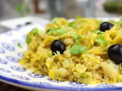 Delicioso bacalao a bras, un plato tradicional con patatas finas, huevo y aceitunas negras, adornado con perejil fresco.