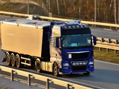 Niebieska ciężarówka z naczepą jedzie autostradą. Kierowca posiada świadectwo kwalifikacji zawodowej, co pozwala mu na bezpieczne przewożenie towarów.