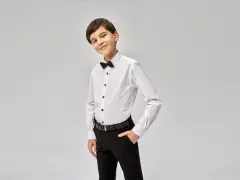 Elegancki chłopiec w białej koszuli z czarną muszką i spodniach. Idealny przykład, jak ubrać chłopca do komunii.