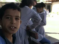 Un garçon souriant pose devant des filles en uniforme dans la même cour d'école.