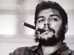 Portrait en noir et blanc de Che Guevara, cigare aux lèvres, regard intense. L'image évoque sa légende, même après sa mort.