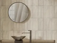 Un lavabo moderne et un miroir rond se reflètent sur un mur de toilette carrelage aux tons sable.