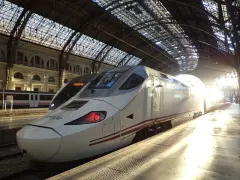 Biały pociąg Renfe, najszybszy pociąg w Europie, stoi na dworcu pod szklanym dachem, oświetlony promieniami słońca.