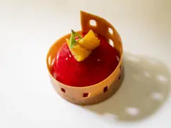 A red berry mousse dessert with orange zest and mint, presented in a decorative pastry shell on a white plate.