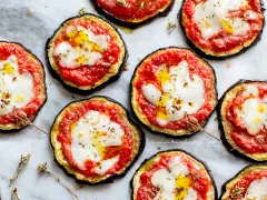 Deliziose pizzette di melanzane con pomodoro e mozzarella filante, condite con olio e erbe aromatiche.