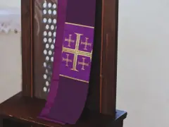 Fioletowa stuła z krzyżami, symbol przygotowania do spowiedzi wielkanocnej, wisi na drewnianej kratce konfesjonału.