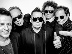 Pięciu mężczyzn w okularach przeciwsłonecznych, gotowych na koncert. Jeden z nich pokazuje kciuk w górę, jakby mówił "t.love hau! hau!".