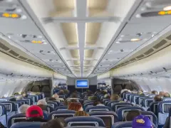 Wnętrze samolotu Boeing 737 Ryanair. Pasażerowie siedzą w rzędach niebieskich foteli, patrząc w stronę kokpitu.