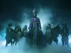 Le groupe de musique Ghost, avec son leader en tenue papale violette, entouré de musiciens aux costumes squelettiques et masqués, émerge d'une brume bleutée.