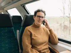 Kobieta w brązowym swetrze rozmawia przez telefon w pociągu. Czas na moją kolej, by usiąść przy oknie i podziwiać widoki.
