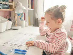 Mała dziewczynka z zapałem uczy się literek dla 3 latka. Na biurku ma kolorowanki z alfabetem i flamastry.