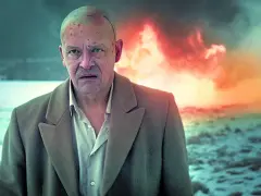 Jan Frycz w dramatycznej scenie, jak z najlepszych filmów i seriali. W tle płomienie, na głowie ślady walki.