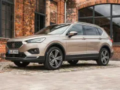 Beiger Seat Tarraco vor Backsteinhaus. Keine Seat Tarraco Probleme hier, nur stilvolles Fahren.