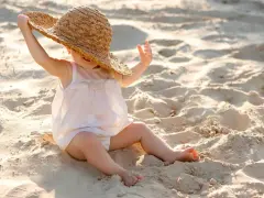 Liten bebis med stråhatt på stranden, njuter av solens värme.