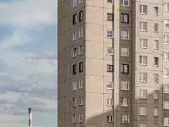 Szare bloki mieszkalne, każde mieszkanie od miasta z oknami wychodzącymi na niebo. W oddali widać komin.