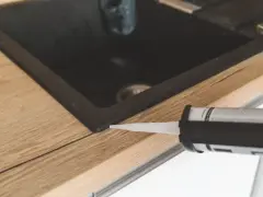 Pistolet z silikonem aplikuje uszczelnienie wokół zlewu, pokazując, jak polożyć silikon na blacie kuchennym.
