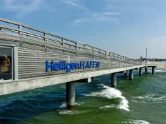 Hol dir die besten heiligenhafen tipps! Die Seebrücke mit dem Schriftzug "Heiligenhafen" ragt ins grüne Meer.