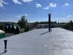 Nowy dach z doskonałą hydroizolacją, gotowy na każde warunki. W tle budynki przemysłowe i błękitne niebo z chmurami.