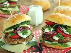Dwa soczyste burgery wołowe z dodatkami na drewnianym tle.