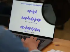 Osoba pracuje przy laptopie, na ekranie widoczne są wykresy fal dźwiękowych, co może być związane z tworzeniem adlibów.