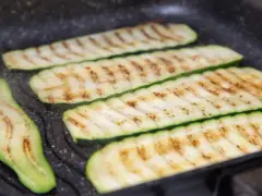 Fette di zucchine grigliate che cuociono su una piastra, con segni di grigliatura dorati e invitanti.