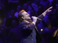 Bono z U2 śpiewa na koncercie, zapowiadając u2 nowa płyta. Tłum w ciemnościach reaguje na jego występ.