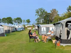 Familj njuter av en solig dag på en av Sveriges billiga campingar. Husvagnar och tält står uppradade på en grön gräsmatta.