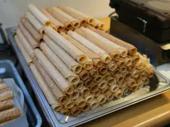 Stos kupnych wafli do rurek z kremem, obok gorącej gofrownicy.