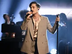 Un cantante con un completo gessato e camicia satinata, microfono in mano, incarna il **dandy significato** con stile sul palco.