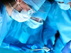 Chirurdzy w niebieskich fartuchach i maskach operacyjnych podczas zabiegu.