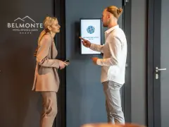 Elegancka para dyskutuje przy hotelowym ekranie. Ona w beżowym garniturze, on w białej koszuli. Idealny strój na śniadanie w hotelu.