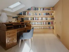 Scrivania in legno massiccio e libreria moderna illuminata, un perfetto esempio di come abbinare e mischiare arredamento classico e moderno in uno studio mansardato.
