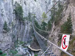 Un emozionante ponte tibetano in Piemonte attraversa una gola rocciosa, con un torrente sottostante e pini aggrappati alle pareti.