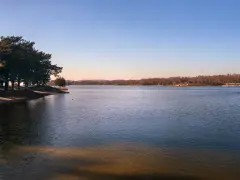 Spokojne jeziora w Małopolsce o zachodzie słońca. Drzewa na brzegu rzucają długie cienie na piaszczystą plażę.
