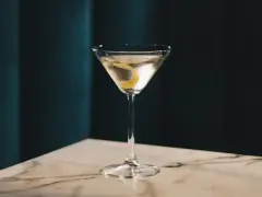 Elegancki gin z wermutem, ozdobiony skórką cytryny, czeka na stole z marmurowym blatem.