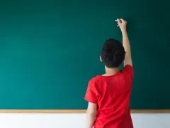 Chłopiec w czerwonej koszulce pisze kredą na zielonej tablicy. Zastanawia się, czy przed "może" stawiamy przecinek.