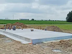 Solidna płyta fundamentowa, gotowa na budowę. Wokół piasek i zielone pola.