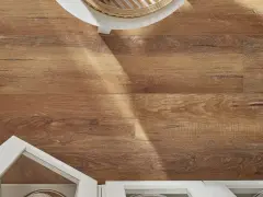 Drewnopodobne panele laminowane czy winylowe tworzą ciepłą podłogę. Widać fragment białej szafki i okrągłego stolika.