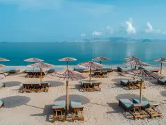 Plaża z leżakami i parasolami, idealna na relaks nad morzem. W oddali widać góry i błękitne niebo.