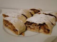 Kilka kawałków pysznego strudla z jabłkami, posypanych cukrem pudrem, czeka na talerzu.
