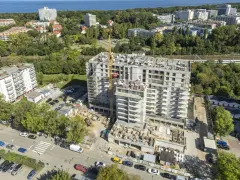 Budowa bloku mieszkalnego w Kołobrzegu. Widok z lotu ptaka na plac budowy, dźwig, samochody i okoliczne budynki. Ceny mieszkań Kołobrzeg mogą być różne.